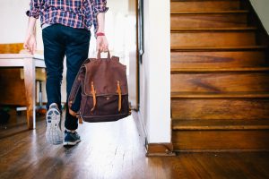 A person walking through a house and holding a brown backpack