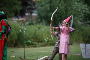 A woman teaching a girl dressed as a medieval princess archery