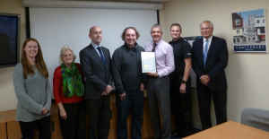 Seven people smiling for a photo with an award certificate