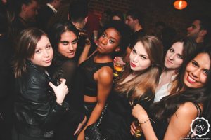 Six young ladies in a club holding drinks and posing for a photo together