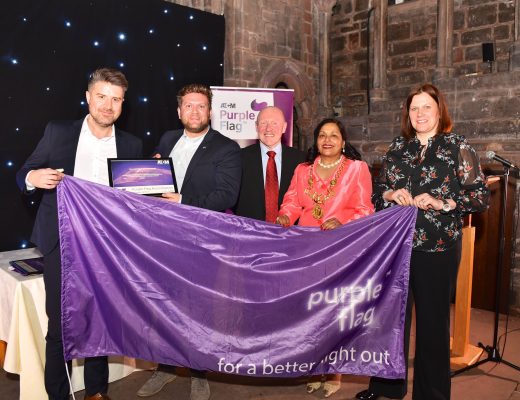 Five people posing and smiling for a photo while holding a ATCCM Purple Flag