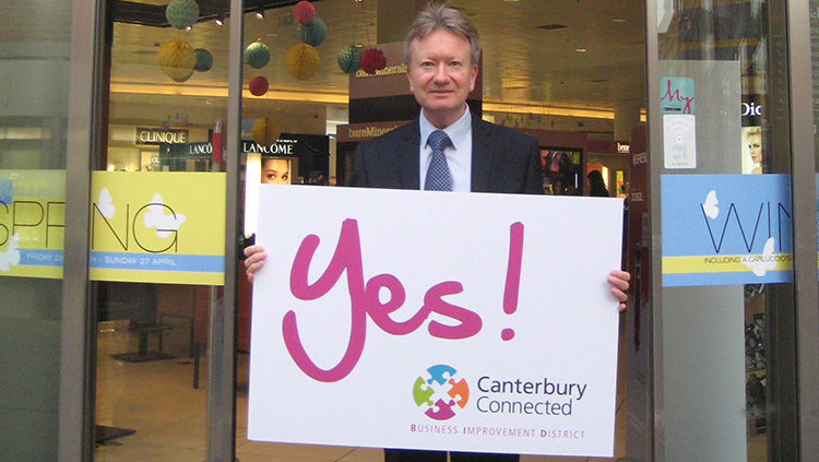 A man outside Fenwick holding a sign that says Yes! Canterbury Connected BID