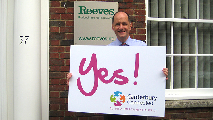 A man outside Reeves holding a sign that says Yes! Canterbury Connected BID