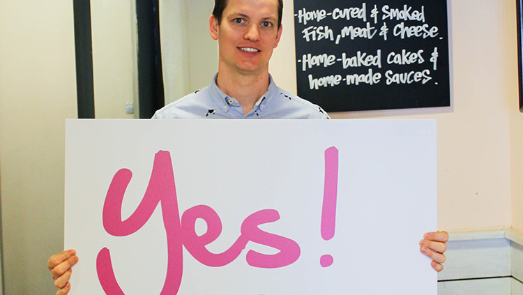 A man in The Refectory holding a sign that says Yes! Canterbury Connected BID