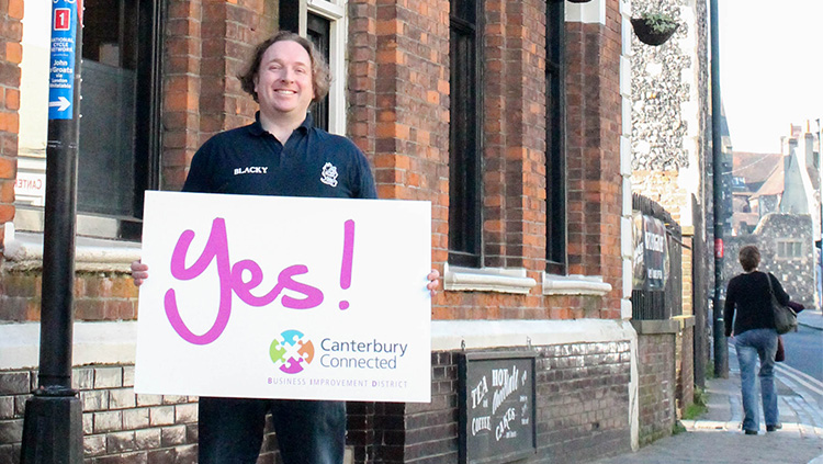 A man outside the Jolly Sailor holding a sign that says Yes! Canterbury Connected BID