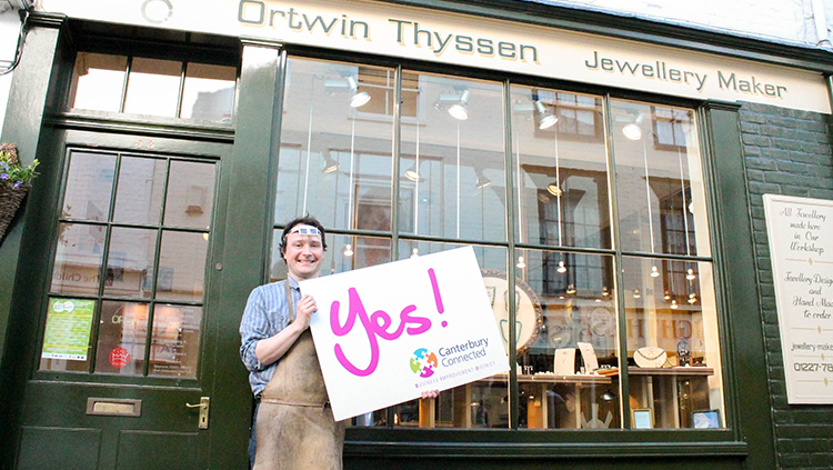 A man outside Ortwin Thyssen holding a sign that says Yes! Canterbury Connected BID