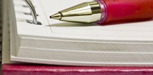A red pen sitting atop a lined notebook