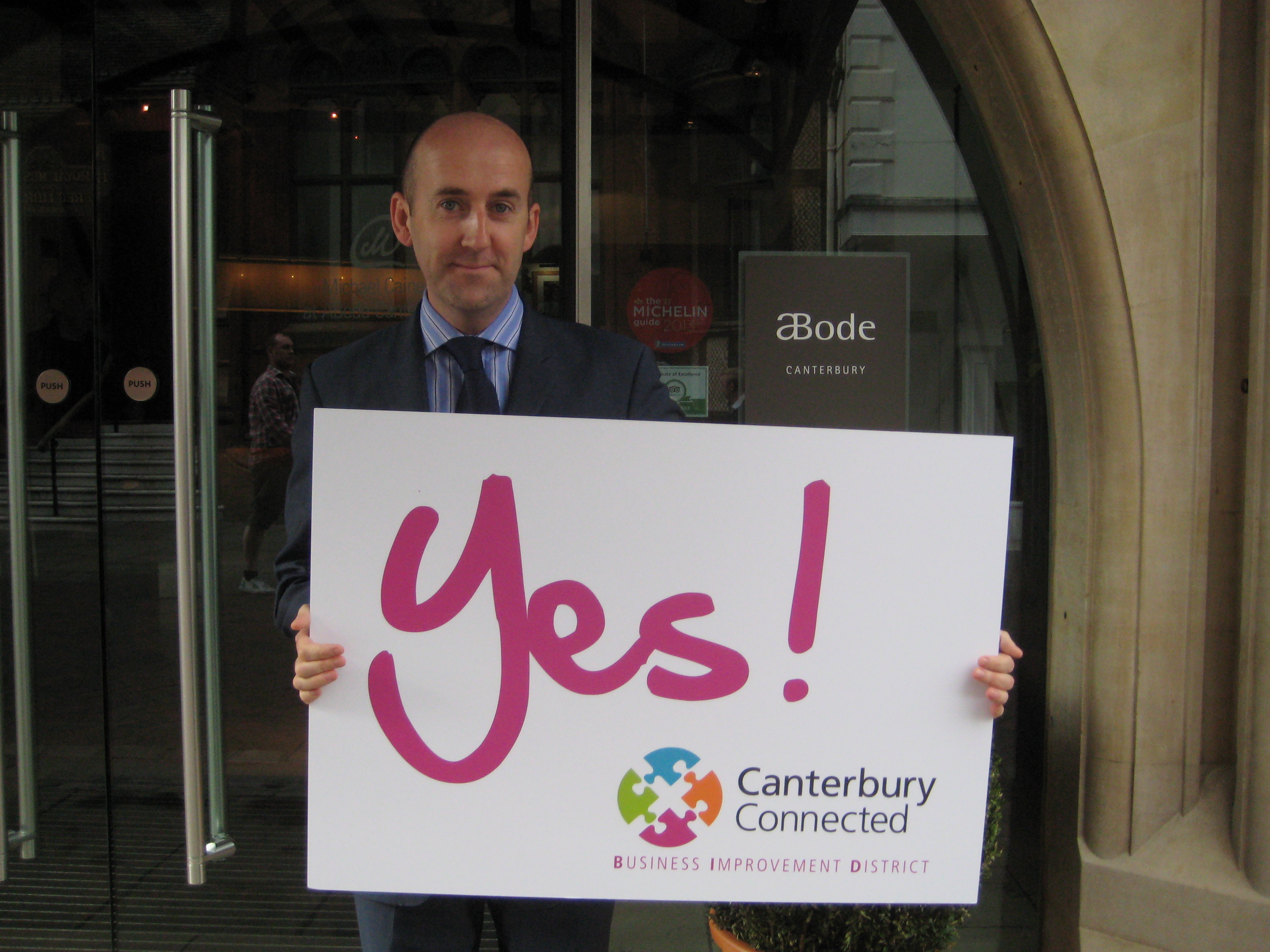 A man outside aBode holding a sign that says Yes! Canterbury Connected BID