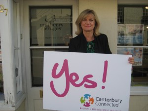 A woman outside Mulberry Cottages holding a sign that says Yes! Canterbury Connected BID