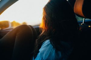 A girl sitting in a car, her knees to her chest and looking out of the window