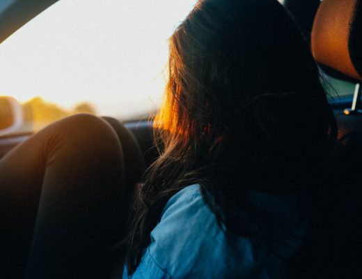 A girl sitting in a car, her knees to her chest and looking out of the window