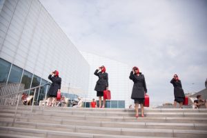 A photo of some ladies in black coats, sunglasses, red headscarves and red briefcases standing on the steps outside The Turner Contemporary Gallery