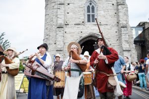 Some people dressed in medieval attire in a parade playing instruments