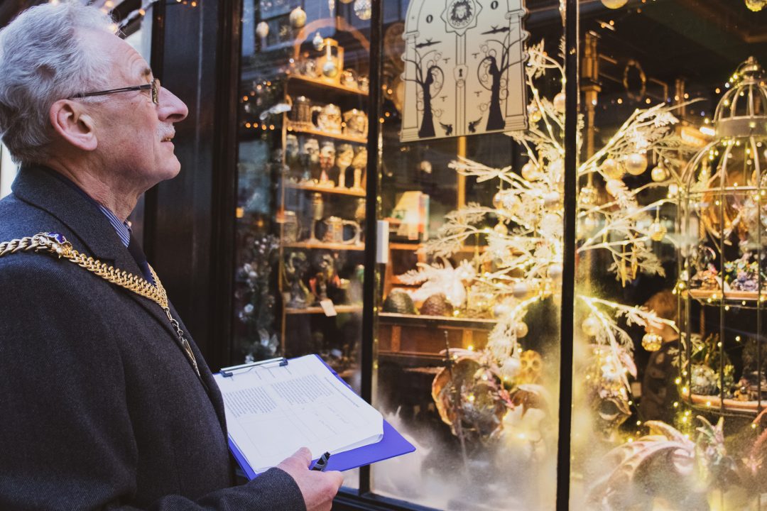 The mayor holding a clipboard and looking in a shop window that is decorated for Christmas