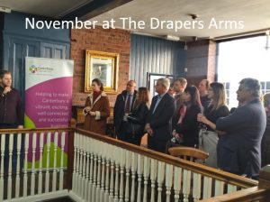 A photo of a room of people listening to a speaker at an event, with text above it that reads November at The Drapers Arms