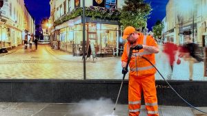 A photo of a man in High-Vis uniform jet washing a pavement