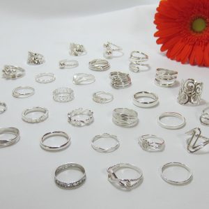 A photo of some silver rings on a white table with a red flower in the background