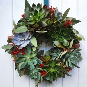 A wreath of holly and succulents on a white door