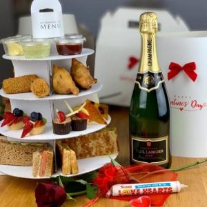 A selection of baked goods and sandwiches on a cake stand alongside a bottle of champagne