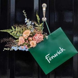 A Fenwick bag with a flower arrangement in it, hanging on a door handle