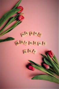 A photo of some tulips and Scrabble letters on a pink table, spelling out Happy Mothers Day