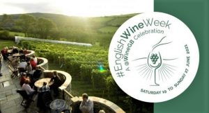 A photo of a vineyard with people seated at tables with a logo for #englishwineweek