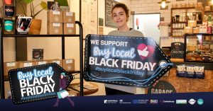 A photo of a woman holding a sign that says we support buy local black friday #buylocalblackfriday