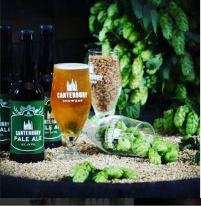 Some photography of some Canterbury pale ale in bottles and glasses displayed on a table with some fake plants