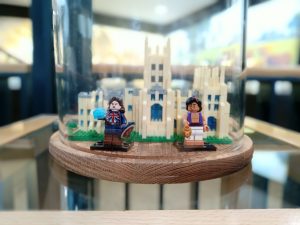 A photo of two Lego figures of Marvel's Captain Britain and Disney's Aladdin, in a glass case standing in front of a small Lego Canterbury Cathedral