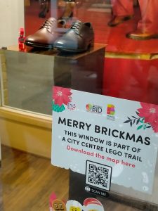 A photo of a shop window with a sign that reads merry brickmas - this window is part of a city centre Lego trail