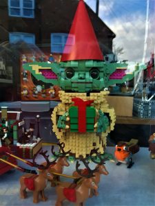 A photo of a Lego baby Yoda holding a gift and wearing a party hat in a shop window