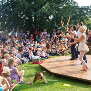 A photo of some performers juggling before a crowd of children