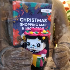 A photo of a statue holding a Christmas shopping map & LEGO trail and a LEGO dia de los muertos figure