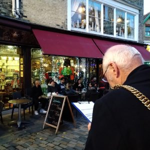 A photo of a mayor, taken from over his shoulder, looking at a piece of paper in front of a shop decorated for Christmas