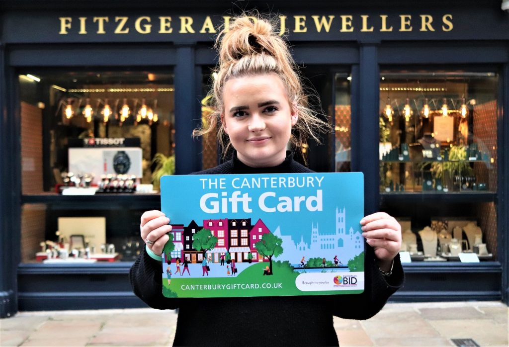 A photo of a young woman holding a sign for the Canterbury Gift Card outside of Fitzgerald Jewellers