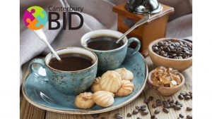 A photo of coffee and biscuits on a table with the Canterbury BID logo over it