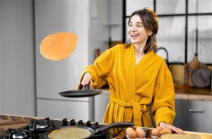 A photo of a woman in the home smiling and flipping a pancake