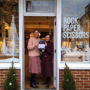 Two women standing and smiling in the doorway of a shop named Rock Paper Scissors