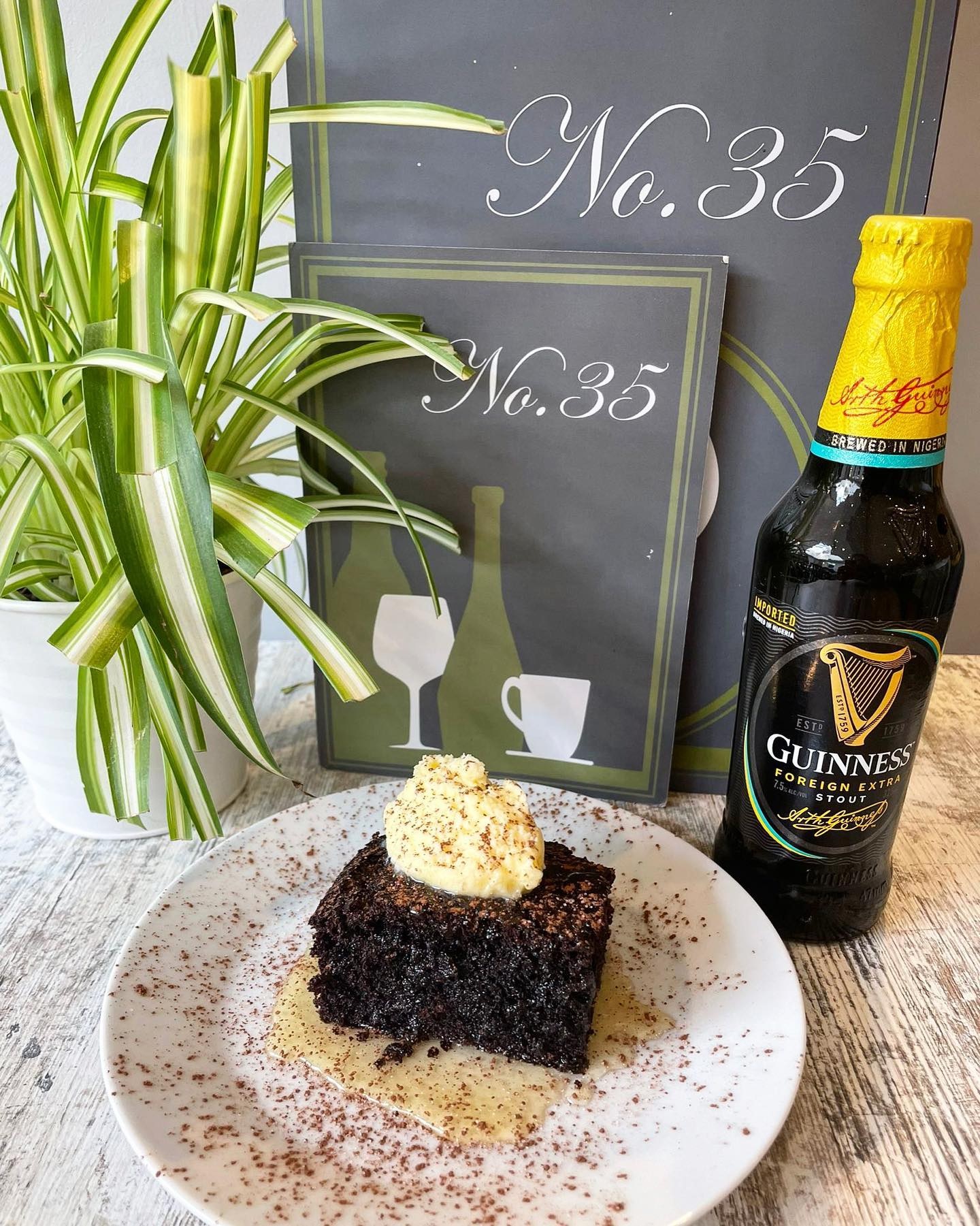 A photo of a plated brownie and ice cream with a glass bottle of Guinness