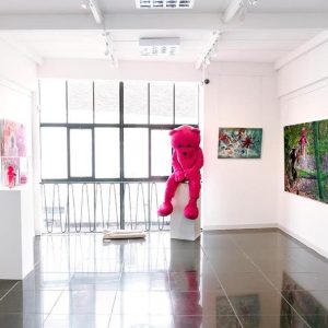 A photo of an art exhibit, with a large pink bear in the centre and other art pieces hung on the walls